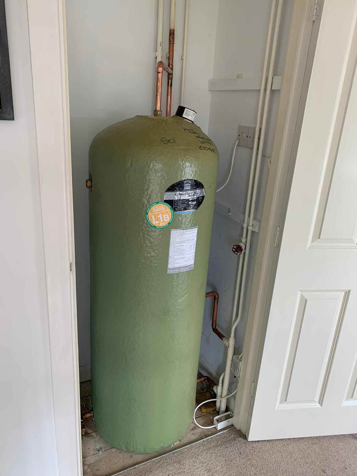 A green hot water cylinder in an airing cupboard