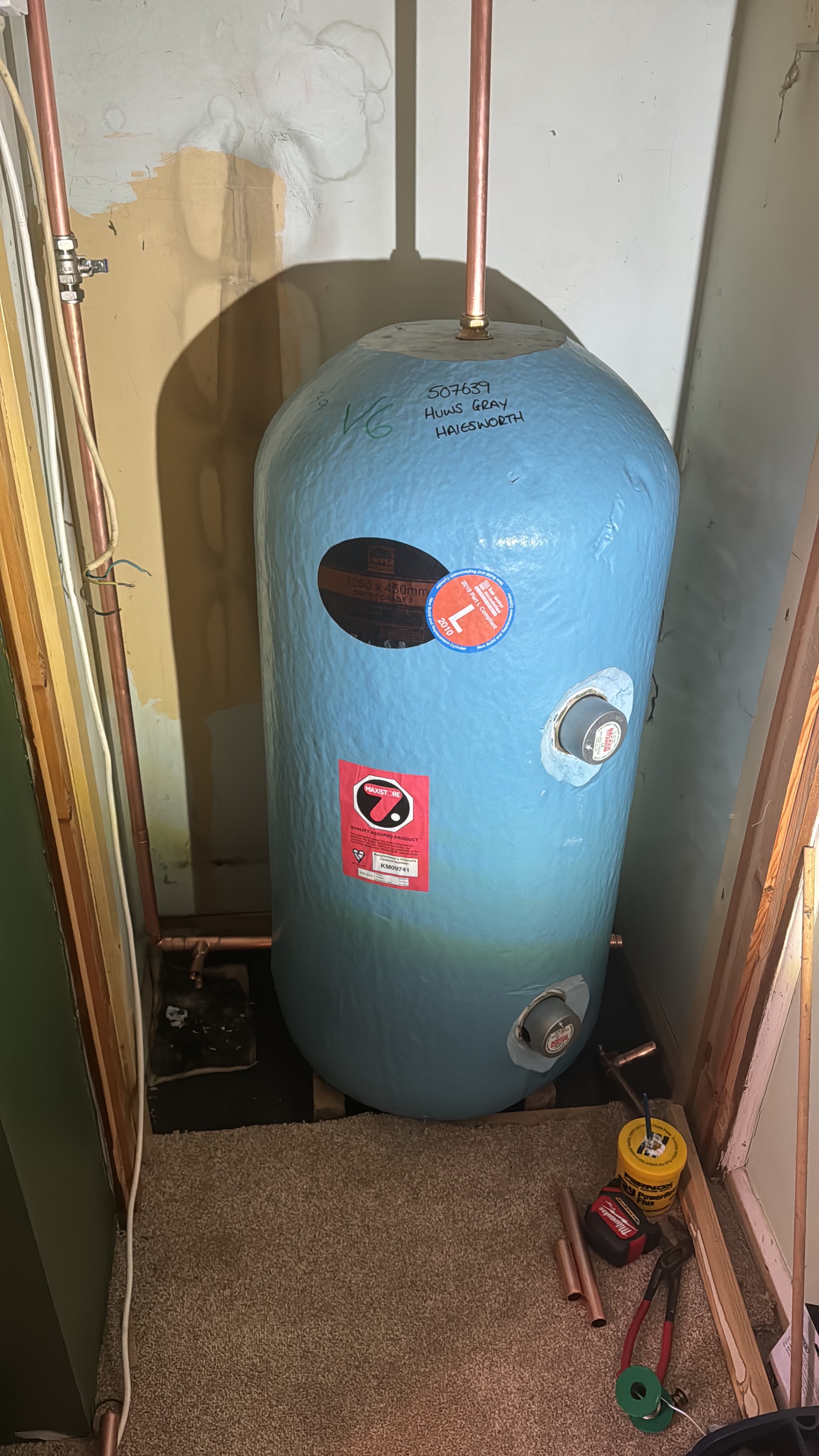 A blue copper hot water cylinder in an airing cupboard, with tools and pipe offcuts on the floor